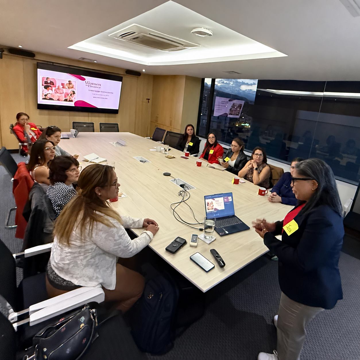 Participantes de Women in Finance reunidas alrededor de una mesa, con la presentación de WIF al fondo.